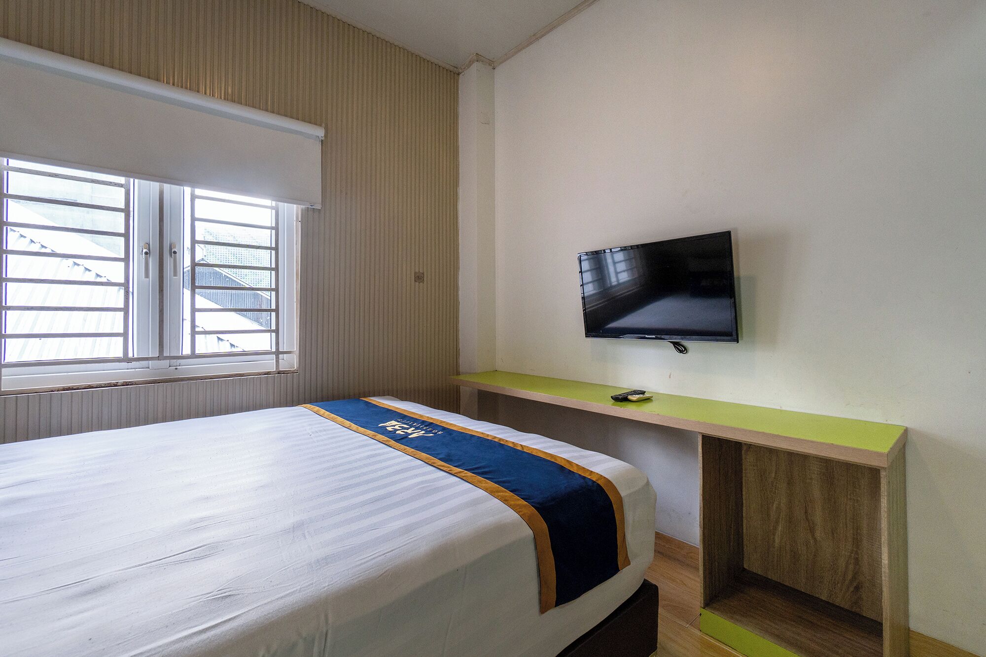Una habitación de hotel con cama, televisor sobre un mueble y ventana con persianas.