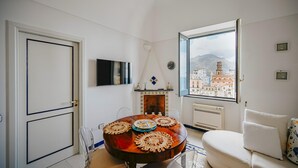 A dining area with a round table, chairs, a fireplace, and a view of a cityscape through a large window. - Casa Blue Torricella by Elite Villas (Atrani)