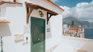 A coastal building with a green door, white walls, and a view of a town with a church and mountains in the background. - Casa Blue Torricella by Elite Villas (Atrani)