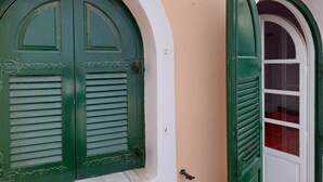 A building with two green doors with shutters, white arches, and a beige wall. - Akrotiri Cosy Studio with Patio and View (Santorini)