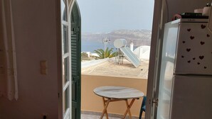 A room with a view of a beach and cliffs, a small table, a refrigerator, and a bed with an orange blanket. - Akrotiri Cosy Studio with Patio and View (Santorini)