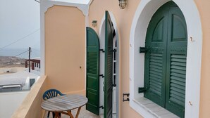 A balcony with a table and chairs, a green door, and a view of the landscape. - Akrotiri Cosy Studio with Patio and View (Santorini)