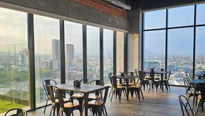 A spacious dining area with large windows offering a city view, modern furniture, and a high ceiling with exposed ductwork. - Loft en Barrio Vergel (Monterrey)