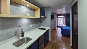 A modern kitchen with a stainless steel sink, wooden shelves, and a view to the living area. - Loft en Barrio Vergel (Monterrey)
