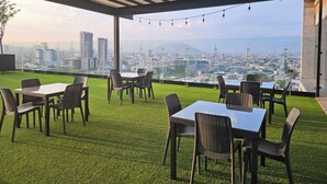 An outdoor seating area with tables and chairs, a grassy floor, and a city view through a glass railing. - Loft en Barrio Vergel (Monterrey)