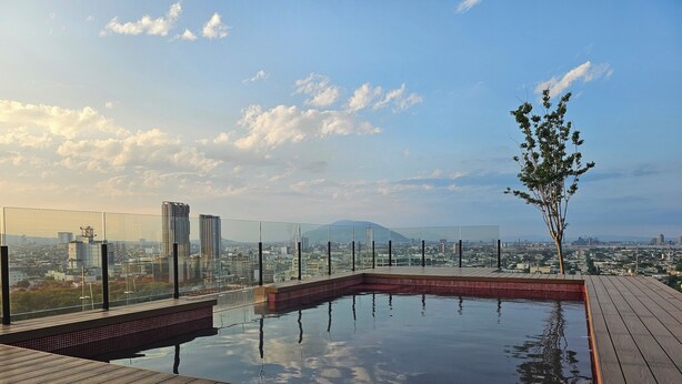 A rooftop infinity pool with a wooden deck, surrounded by glass railings, offering a cityscape view. - Loft en Barrio Vergel (Monterrey)