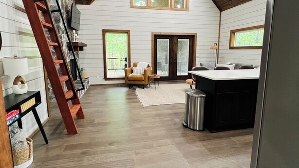 A spacious loft-style room with a high ceiling, wooden beams, and a large window. - Eagle Forest-Sleeps 4, Hot Tub, Fireplace (Broken Bow)
