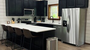 A modern kitchen with dark cabinets, a stainless steel refrigerator, a microwave, and a sink. - Eagle Forest-Sleeps 4, Hot Tub, Fireplace (Broken Bow)