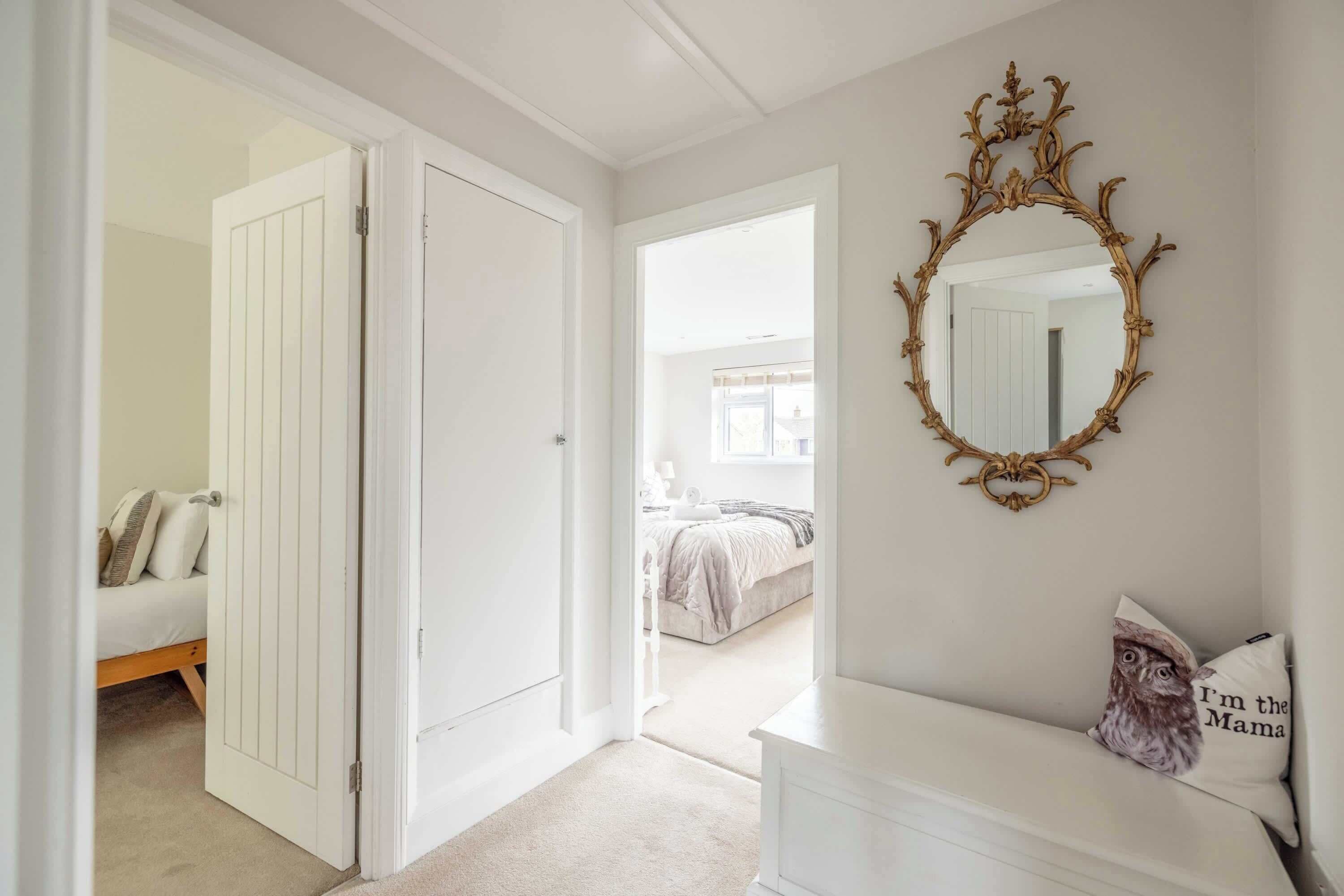 A hallway with a white door leading to a bedroom, a white dresser with a pillow, and a mirror with an ornate frame.