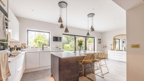 A modern kitchen with a central island, pendant lighting, and a view of the outdoors. - Windsor Charm : Spacious 4-Bed, Parking & Garden (Berkshire)