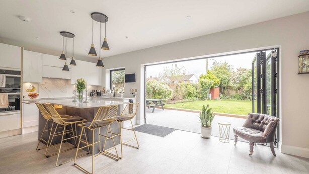 A modern kitchen with a bar area, large windows, and a patio with a chair. - Windsor Charm : Spacious 4-Bed, Parking & Garden (Berkshire)