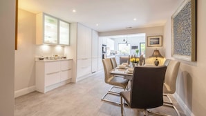 A modern dining area with a table set for two, a kitchen in the background, and a framed artwork on the wall. - Windsor Charm : Spacious 4-Bed, Parking & Garden (Berkshire)