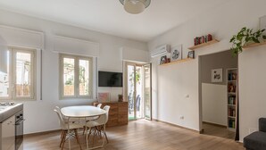 A modern kitchen with white cabinetry, a dining area with a white table and chairs, and a living area with a grey sofa. - S Agostino Apartment w Terrace by Wonderful Italy (Palermo)