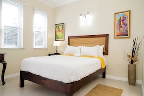 A neatly made bed with white bedding and a yellow throw, a bedside table with a lamp, and two framed artworks on the wall. - Chic Haven Studio in Kingston (Kingston)