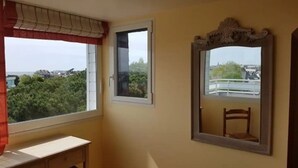 Una habitación con un ventanal grande, un espejo pequeño y una silla de madera.