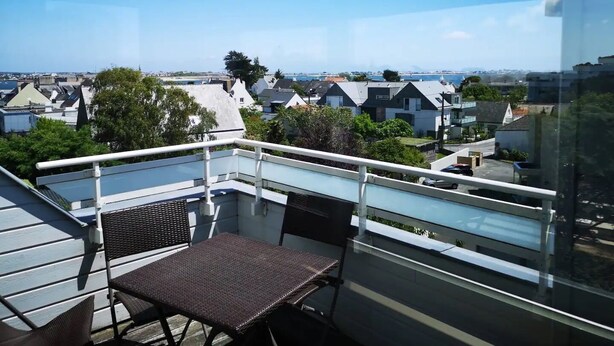 Un balcón con una mesa y sillas, con vistas a una zona residencial con casas y un cielo despejado.
