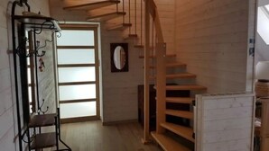 Una escalera de madera que conduce a un piso superior, un perchero metálico con ganchos y una puerta con paneles de vidrio esmerilado.