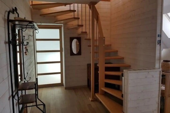 Una escalera de madera que conduce a un piso superior, un perchero metálico con ganchos y una puerta con paneles de vidrio esmerilado.