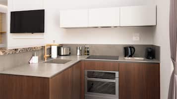 A modern kitchen with a built-in oven, a coffee maker, and a flat-screen TV mounted above the counter.
