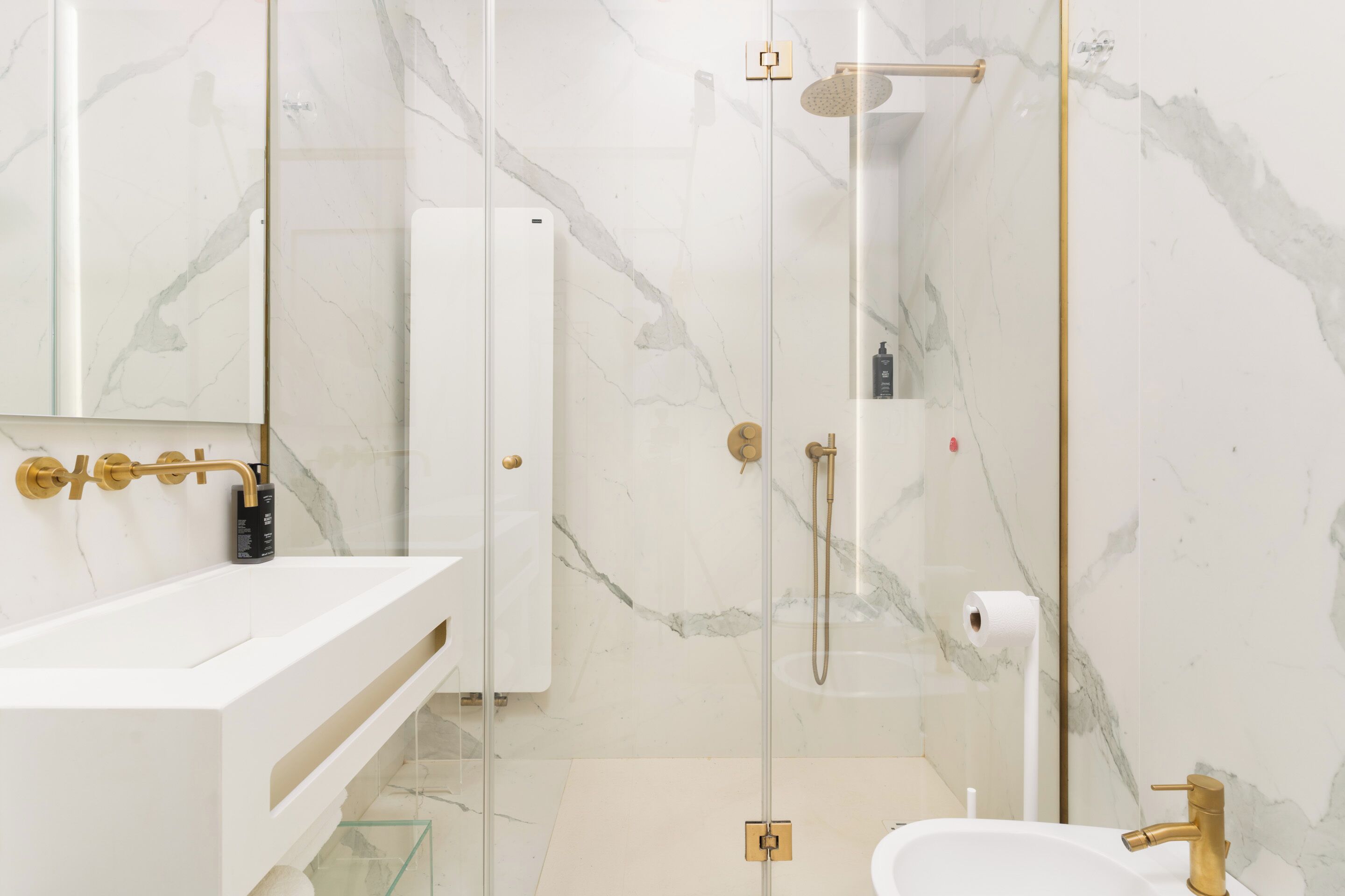 Un bagno moderno con un lavandino bianco, accessori dorati e una cabina doccia in vetro.