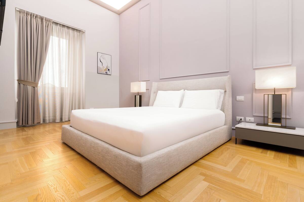 A modern hotel room with a large bed, wooden flooring, and two bedside lamps.