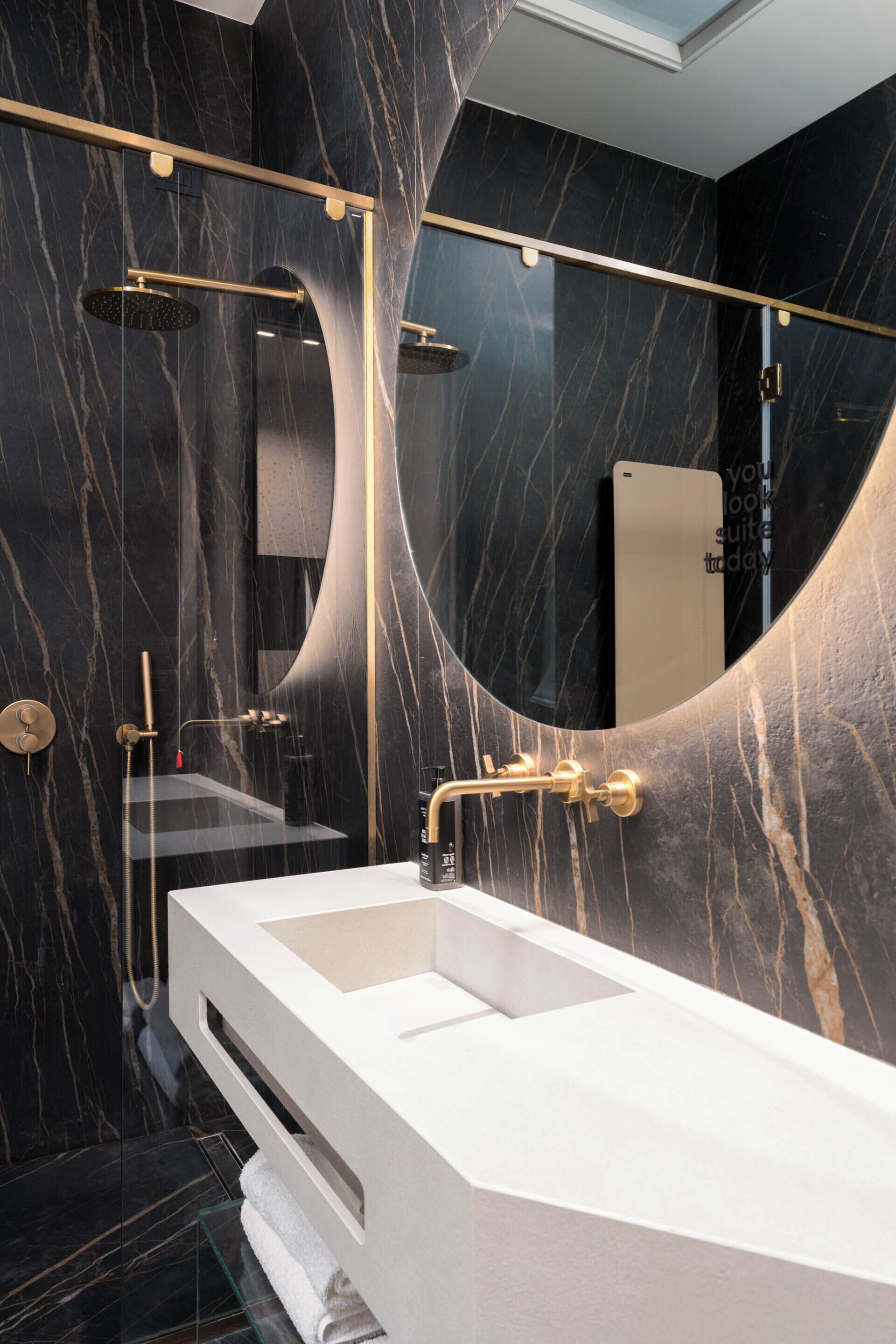 A modern bathroom with a large mirror, a white sink, and a gold showerhead.