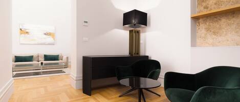 Una sala moderna con un sofá, una mesa de centro de vidrio, un escritorio negro, una silla verde y una lámpara de pie.