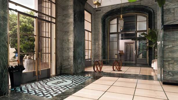 Un vestíbulo amplio con ventanas grandes, piso estampado y una zona de estar con mesa y sillas.