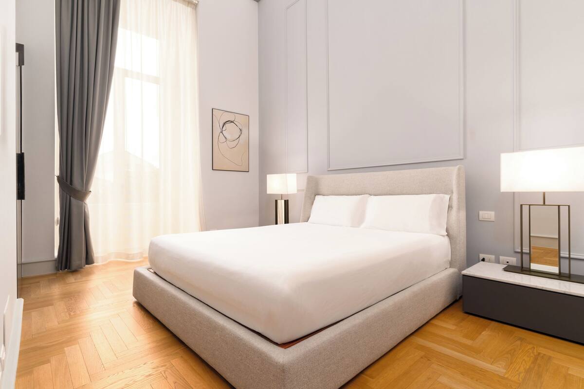 A modern bedroom with a large bed, bedside lamps, and a nightstand.