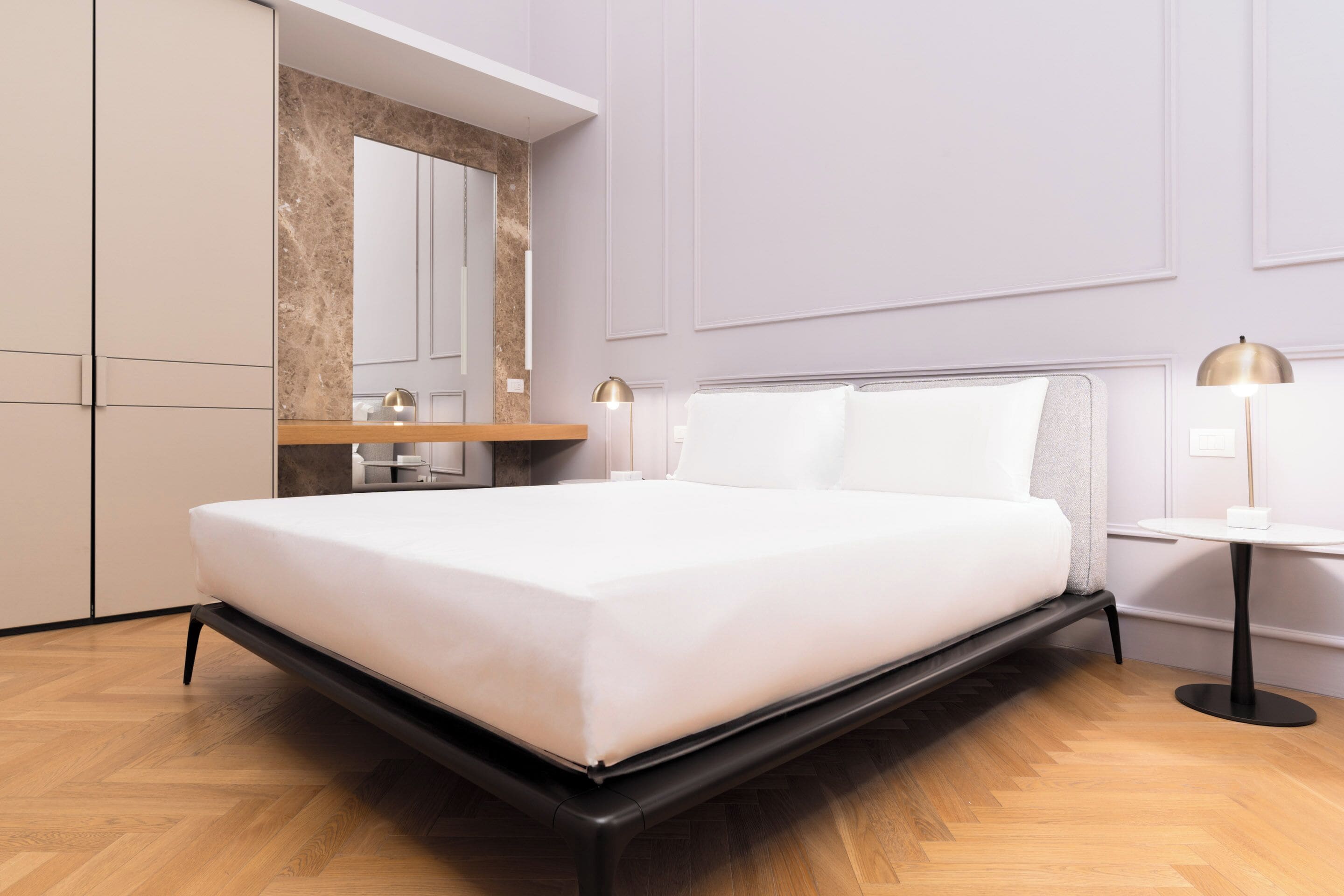 Quarto moderno com cama, mesas de cabeceira, espelho e guarda-roupa.
