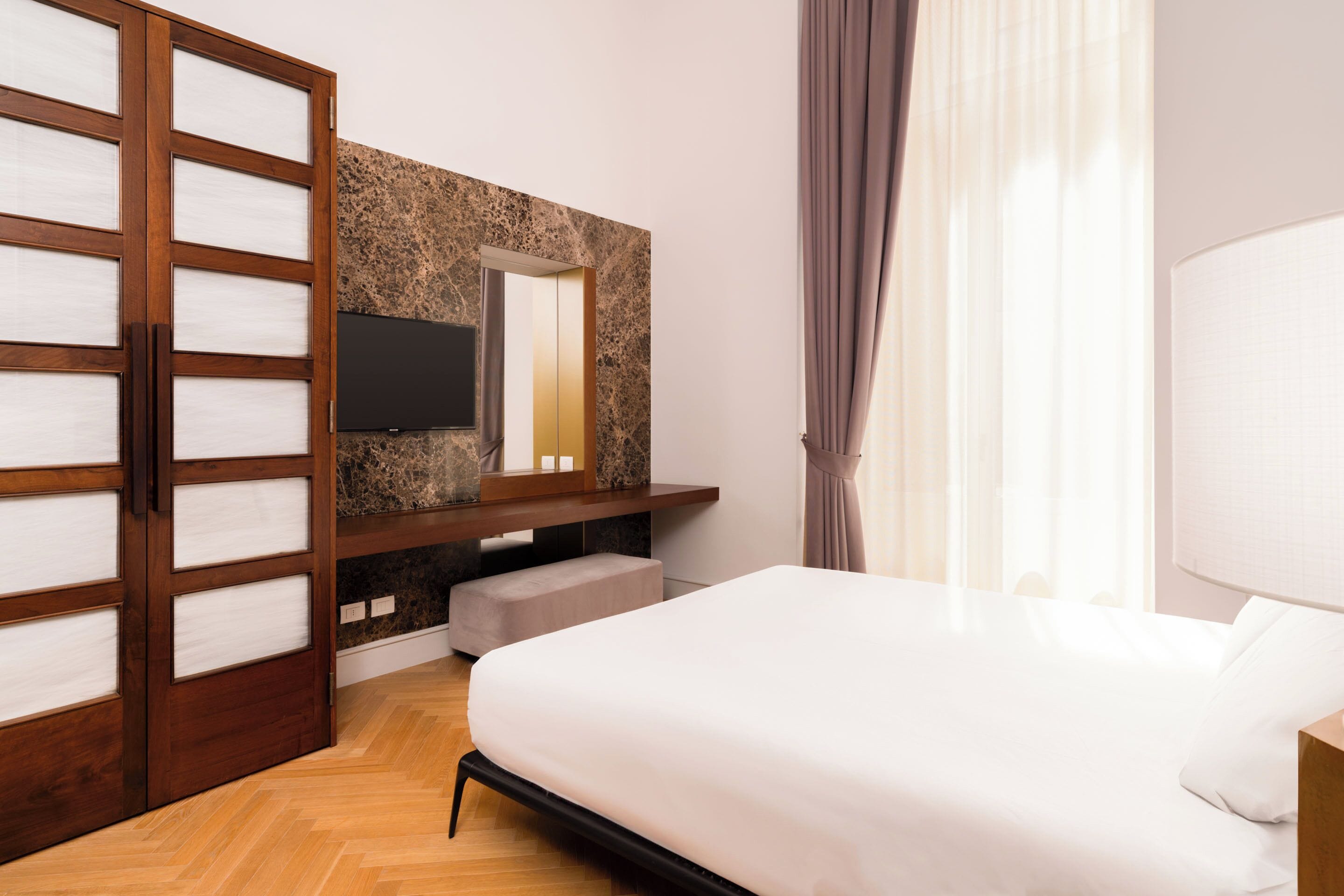 Ein Schlafzimmer mit Bett, Fernseher an einer Steinwand, einem Holzschrank und einem Fenster mit Vorhängen.