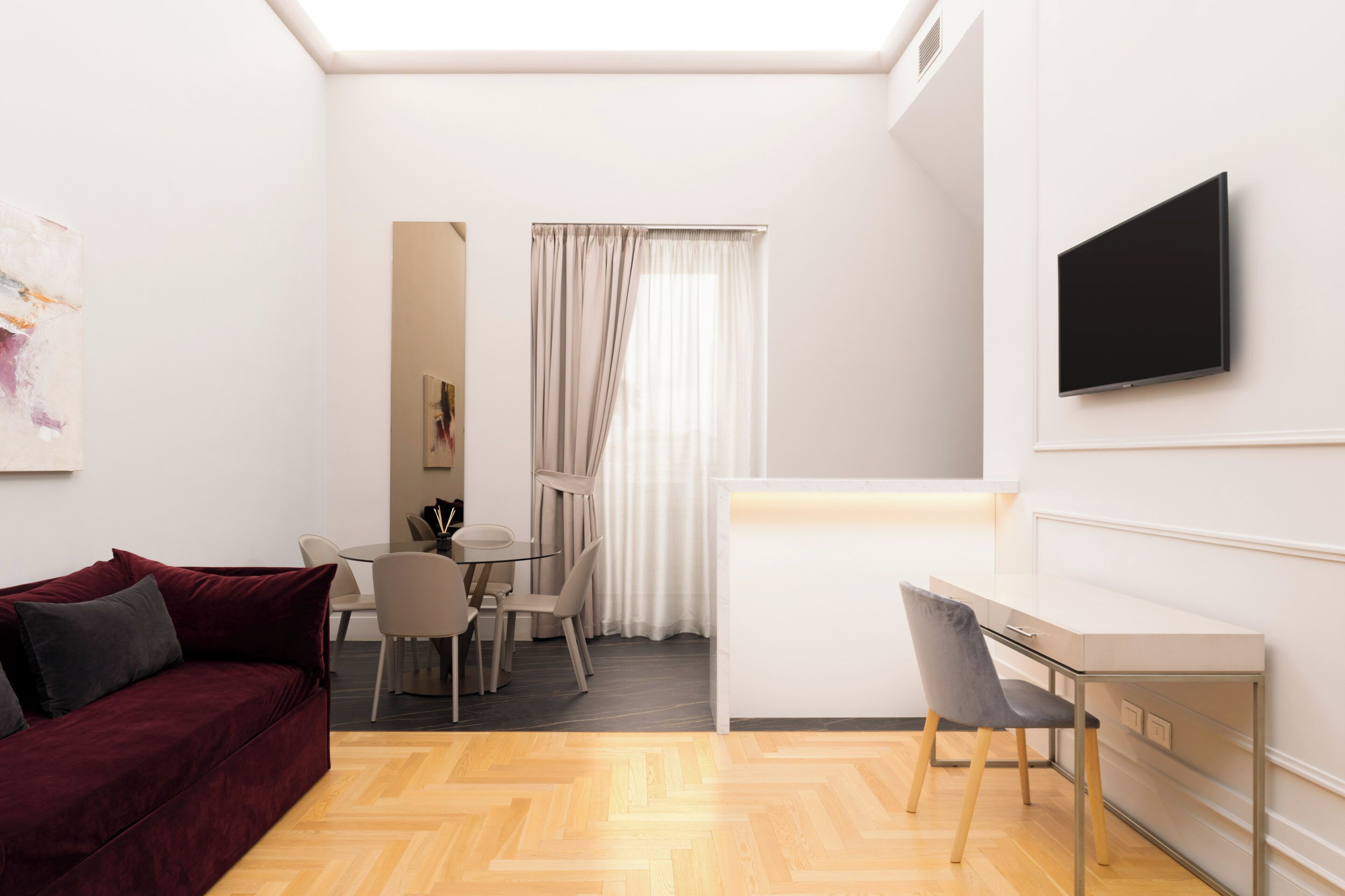 En moderne stue med sofa, spisebord med stole, fjernsyn monteret på væggen og et vindue med gardiner.