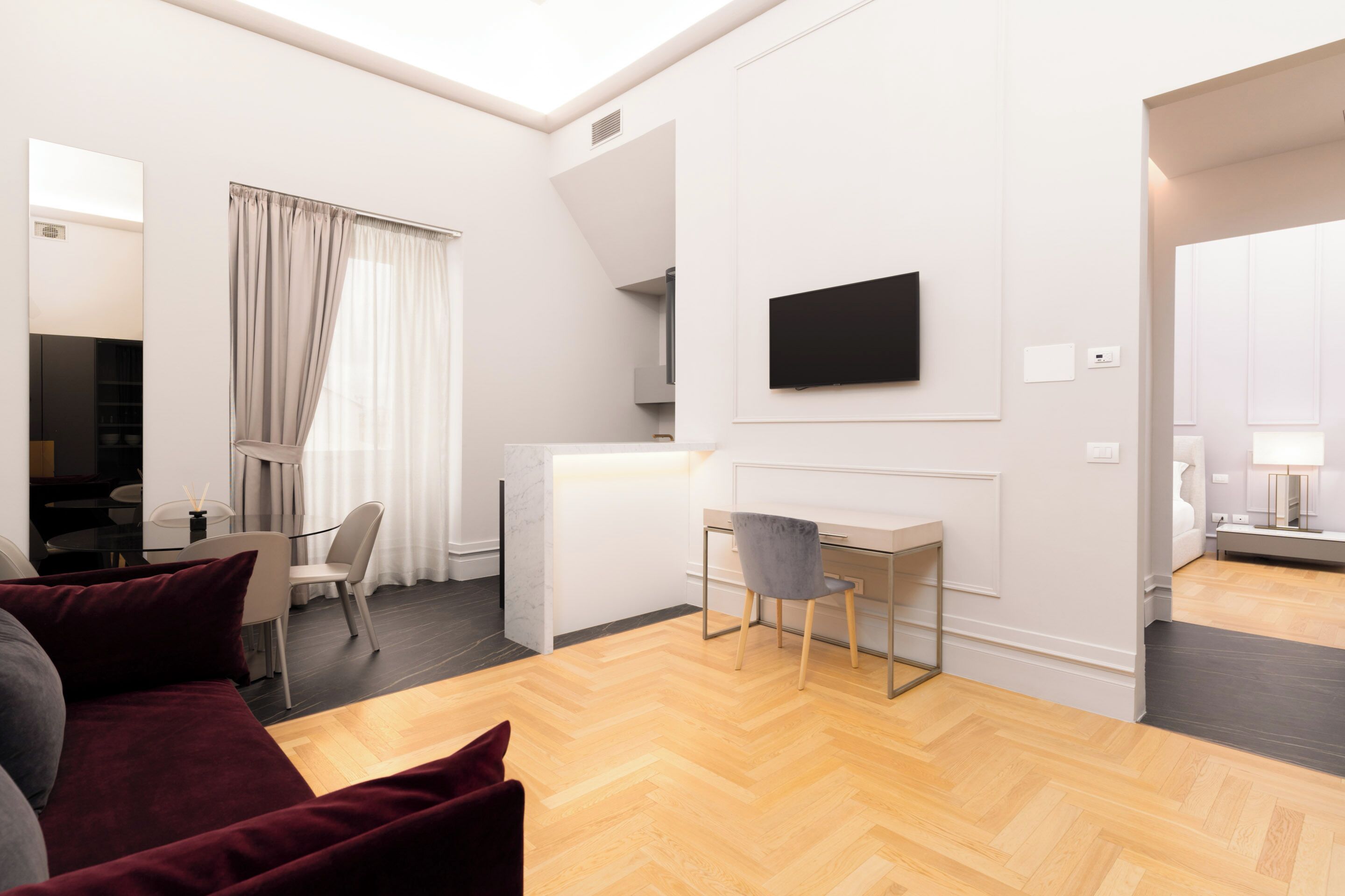 Ein modernes Wohnzimmer mit einer Couch, einem Schreibtisch und einem an der Wand befestigten Fernseher.