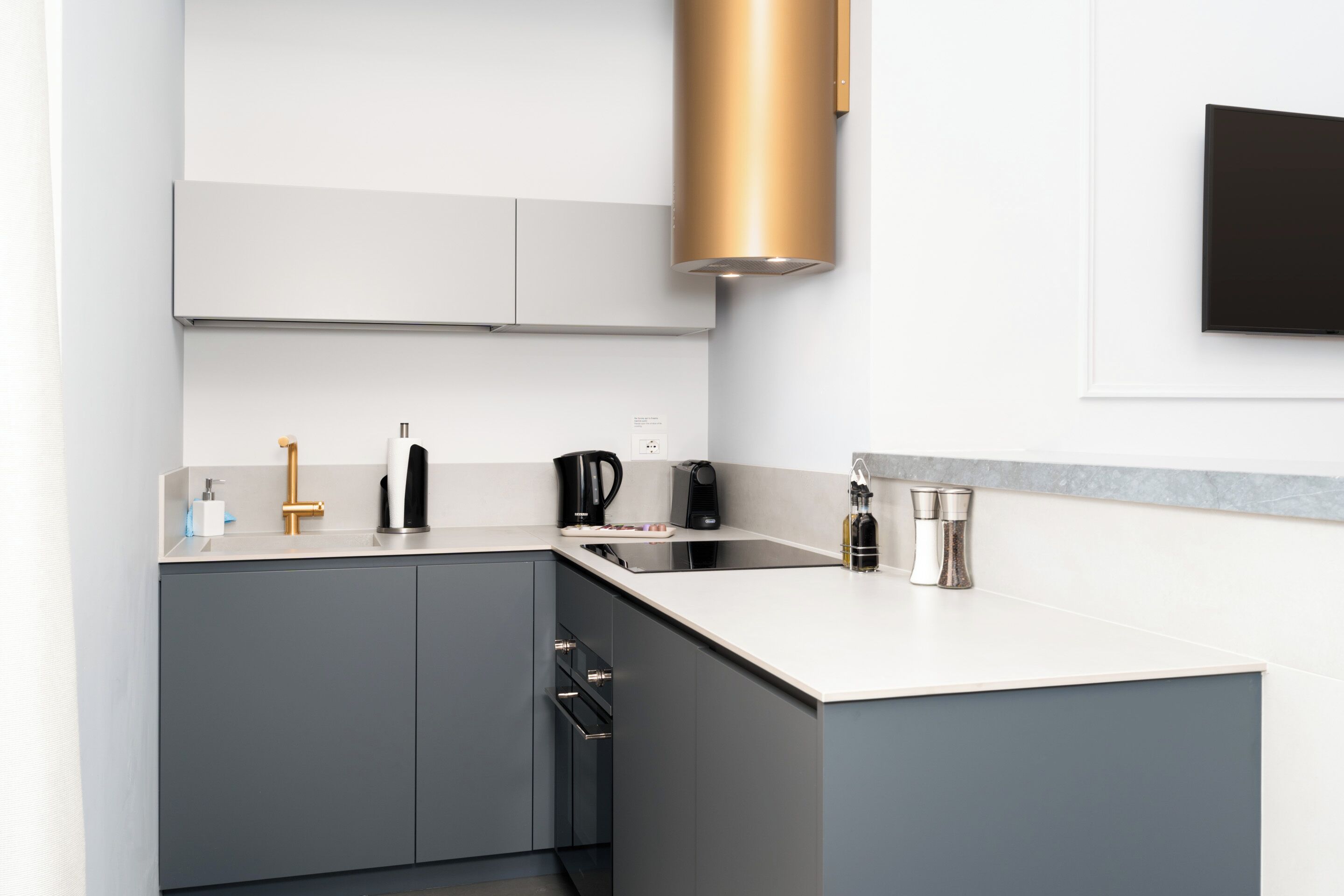 A modern kitchen with grey cabinets, a white countertop, and a gold-colored range hood.