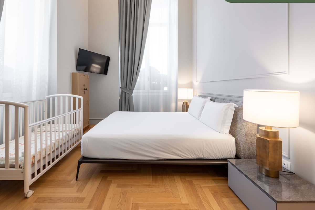 A bedroom with a bed, a crib, a TV mounted on the wall, and a bedside lamp.
