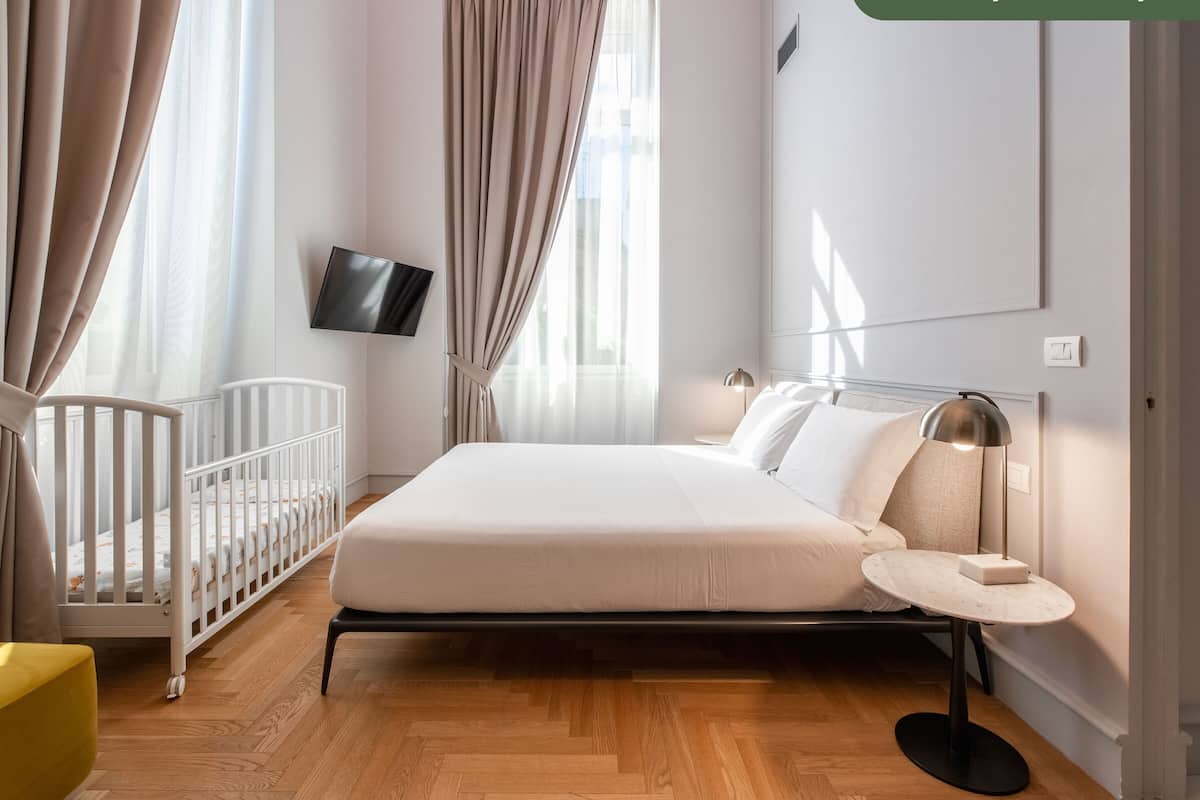 A modern bedroom with a bed, a crib, a round table, and a TV on the wall.