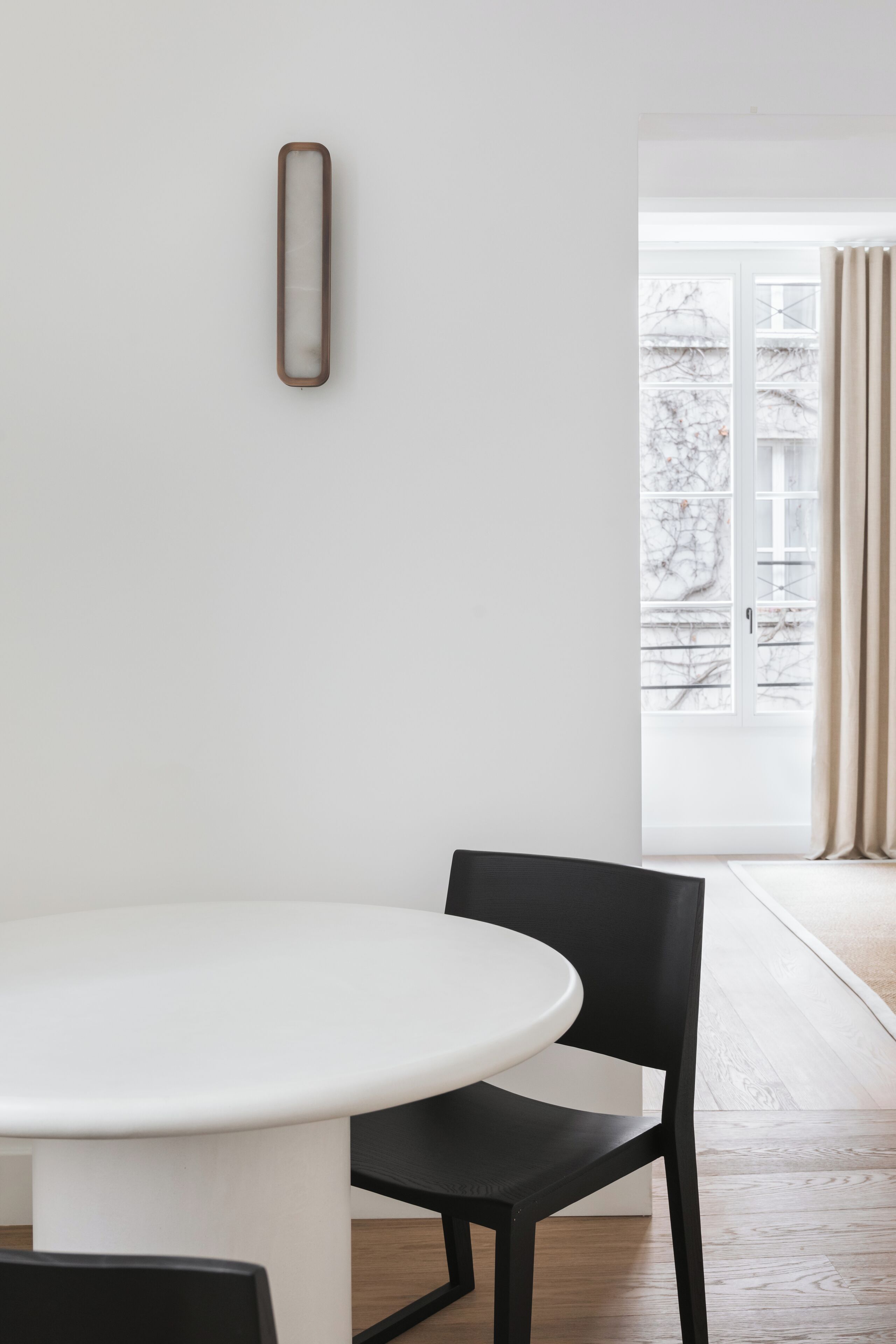 Ein stilvoller Essbereich mit einem runden Tisch und schwarzen Stühlen, einem schlichten Wandbild und einem großen Fenster mit Vorhängen.