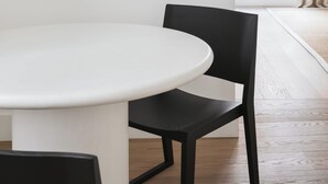 Ett modernt matområde med ett runt bord och svarta stolar, ett minimalistiskt konstverk på väggen och ett stort fönster med gardiner.