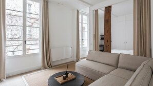 Ett modernt vardagsrum med en beige soffa, ett runt soffbord och ett stort fönster med gardiner.