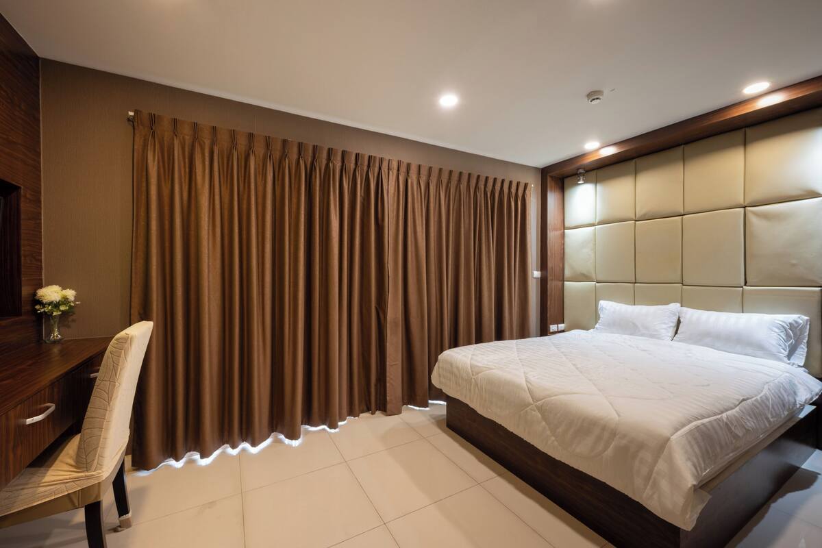 Habitación de hotel con cama, escritorio, silla y un ventanal con cortinas.