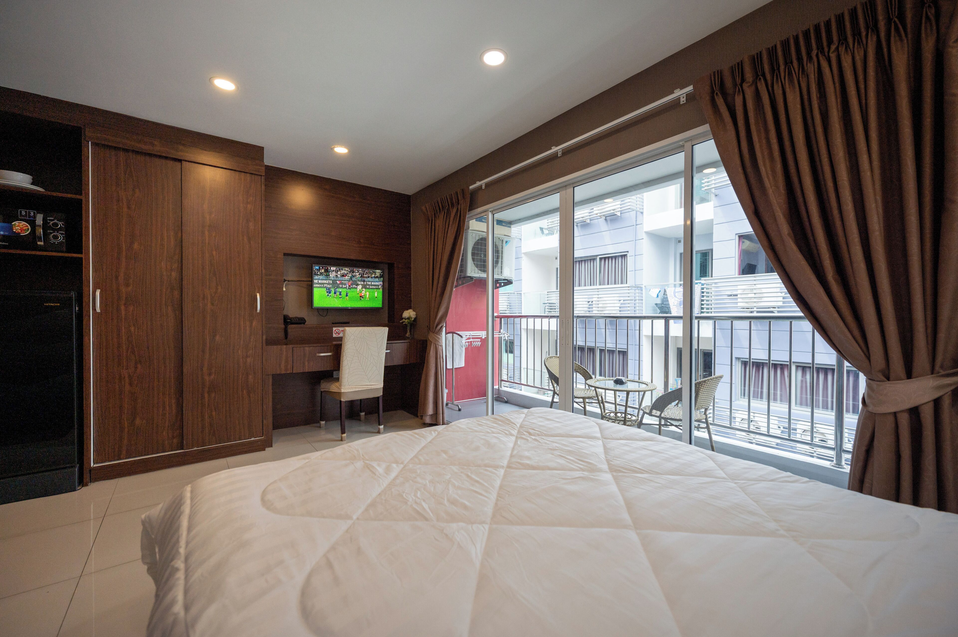 A hotel room with a large bed, a desk with a chair, a television, and a balcony with a view of the outside.