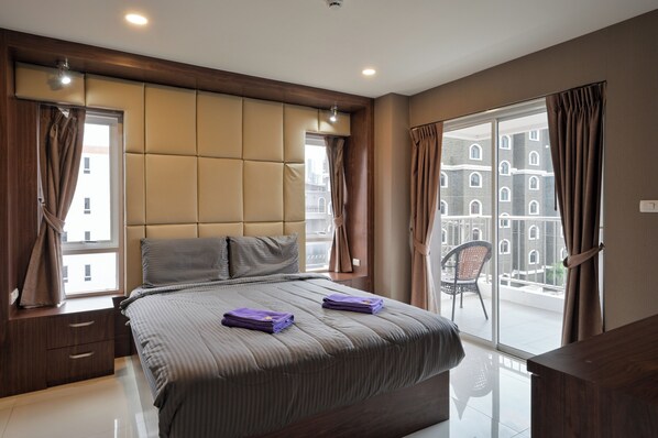 Une chambre moderne avec un grand lit, une vue sur la ville et un balcon agrémenté d’une chaise.