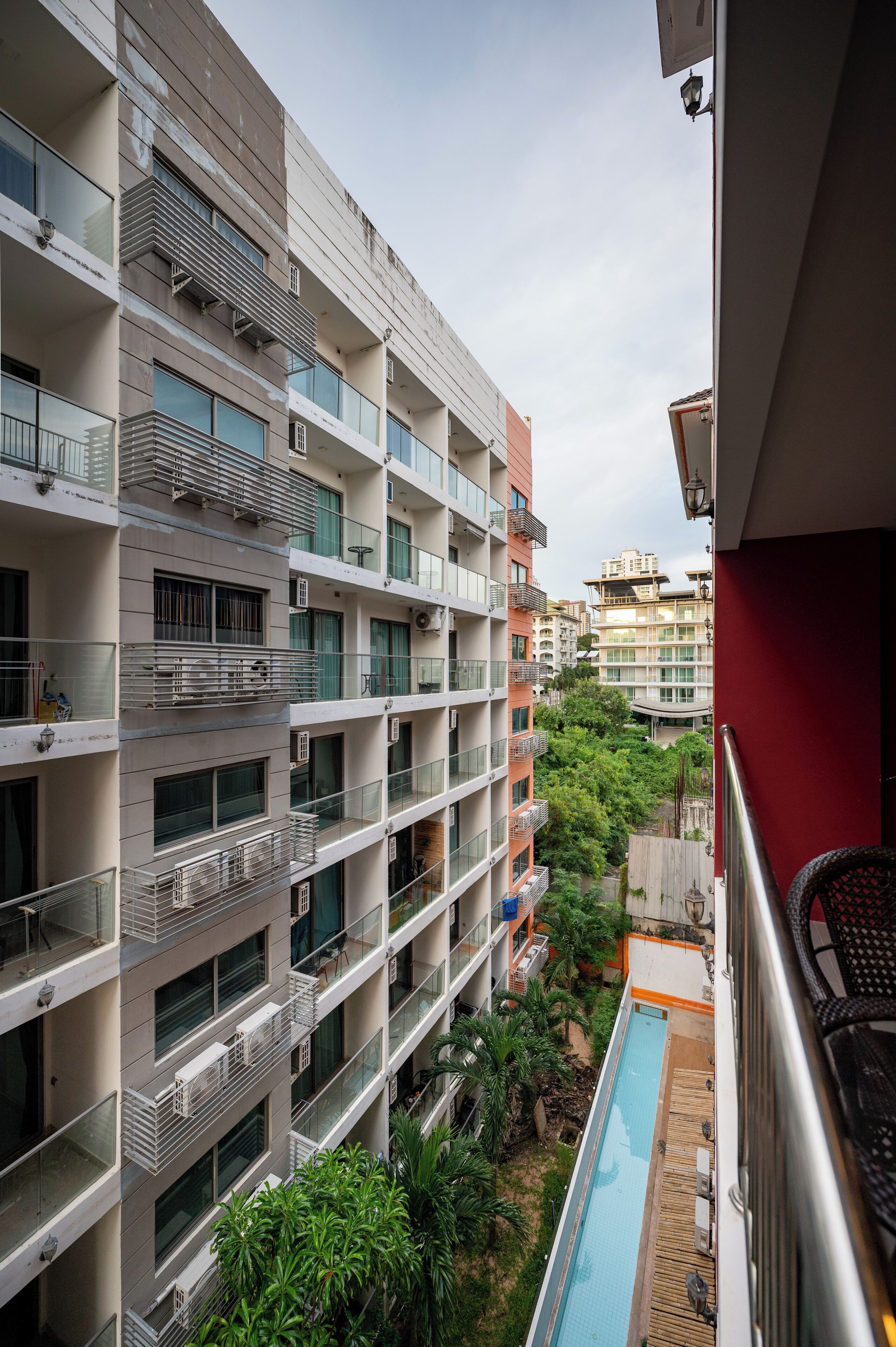 A multi-story residential building with balconies, a swimming pool, and surrounding greenery.