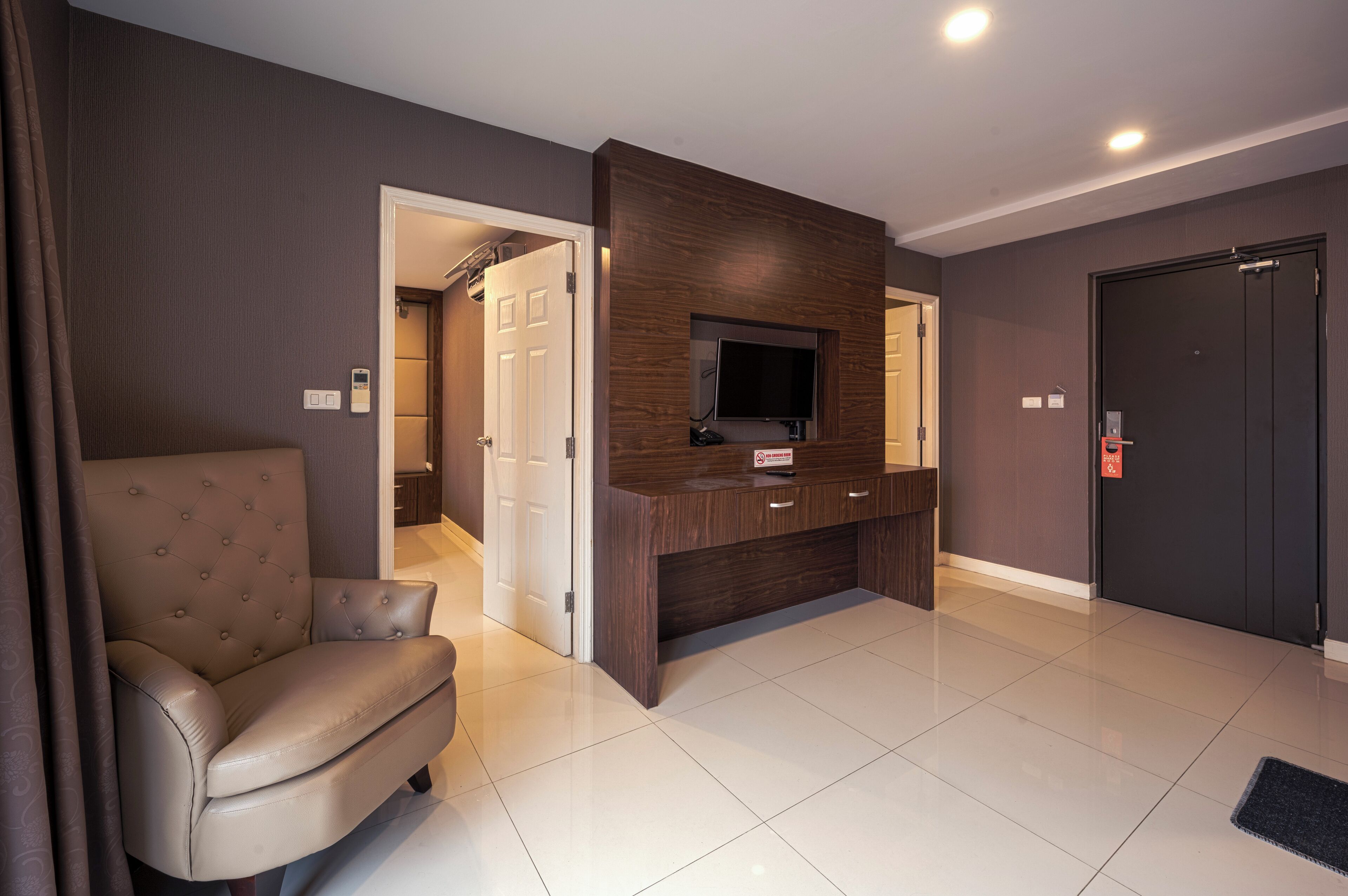Una sala de estar moderna con un sofá de cuero, un televisor de pantalla plana montado en un mueble de madera y una puerta que da a otra habitación.