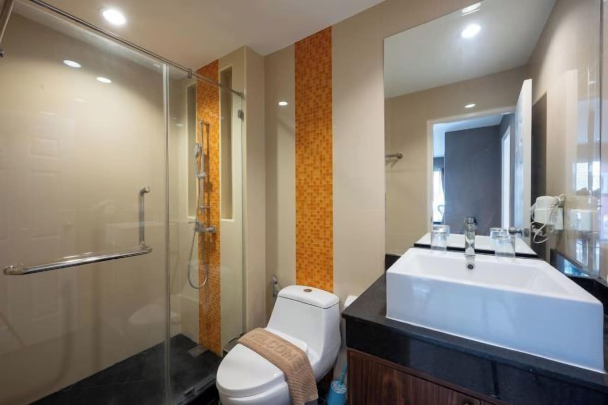 Une salle de bain moderne avec une douche à parois de verre, des toilettes blanches et un grand lavabo surmonté d’un miroir.