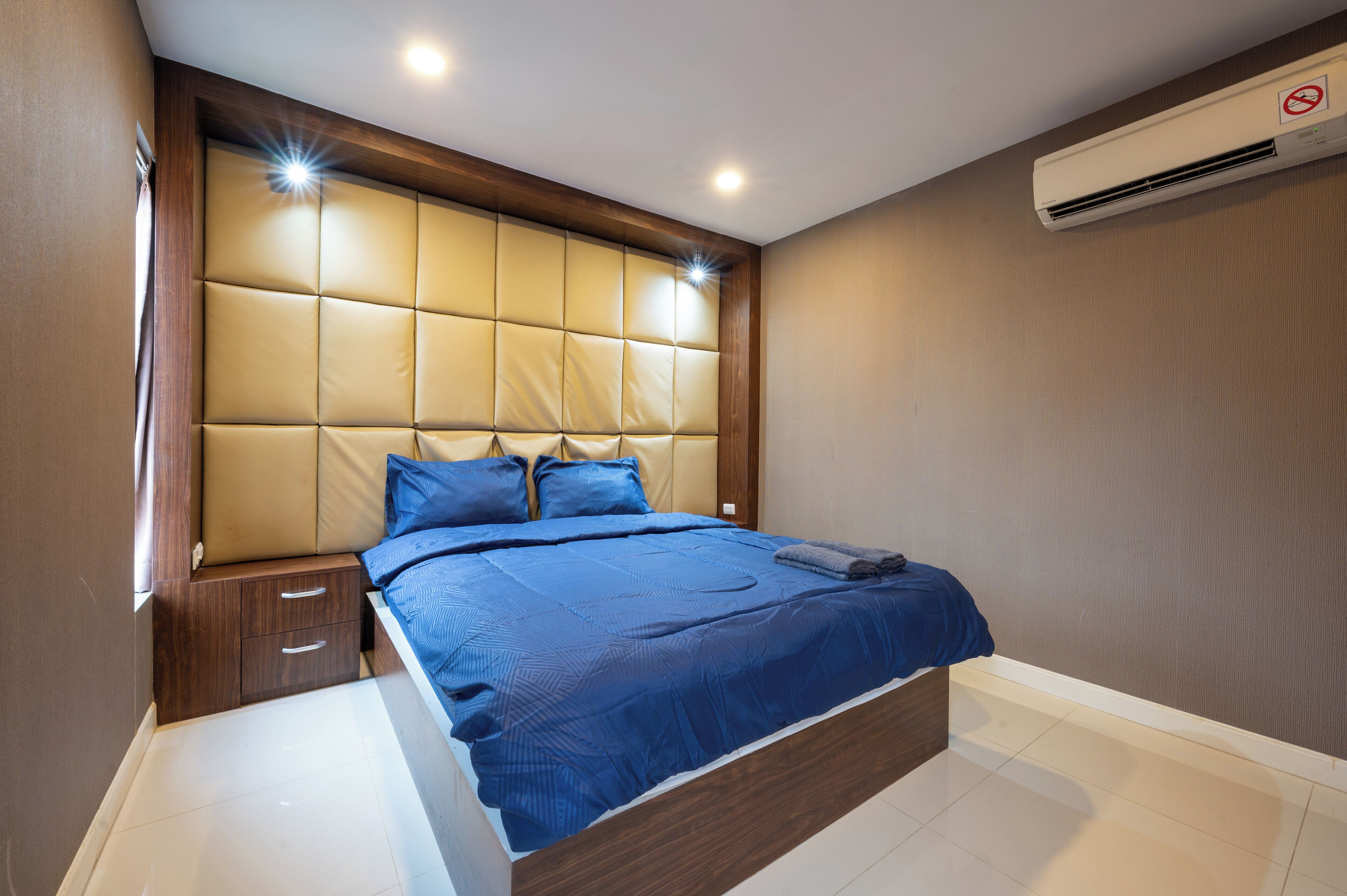 A bedroom with a large bed, a wooden headboard, a nightstand, and an air conditioning unit.