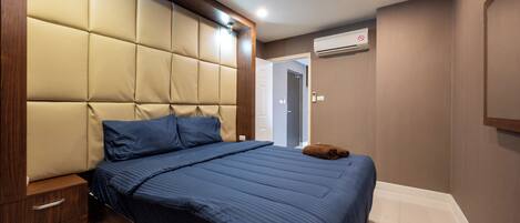 A bedroom with a tufted headboard, a bed with blue bedding, a wooden nightstand, and a wall-mounted air conditioner.