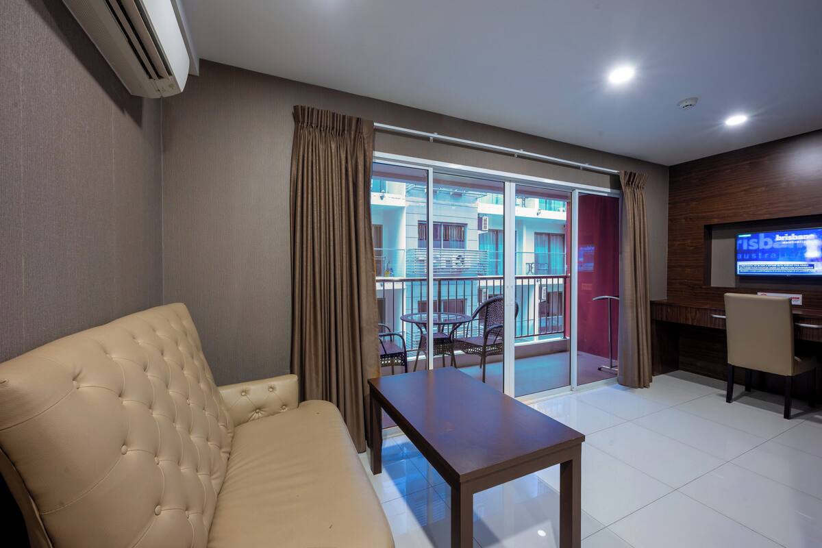 Habitación de hotel con sofá, una mesita, televisor y balcón con vistas a edificios.
