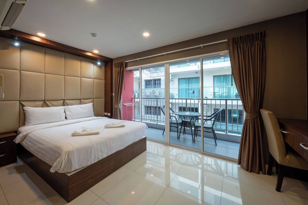Habitación de hotel con una cama grande, un escritorio y un balcón con mesa y sillas.