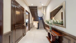 Un couloir avec une porte en bois, un escalier et un miroir fixé au mur.